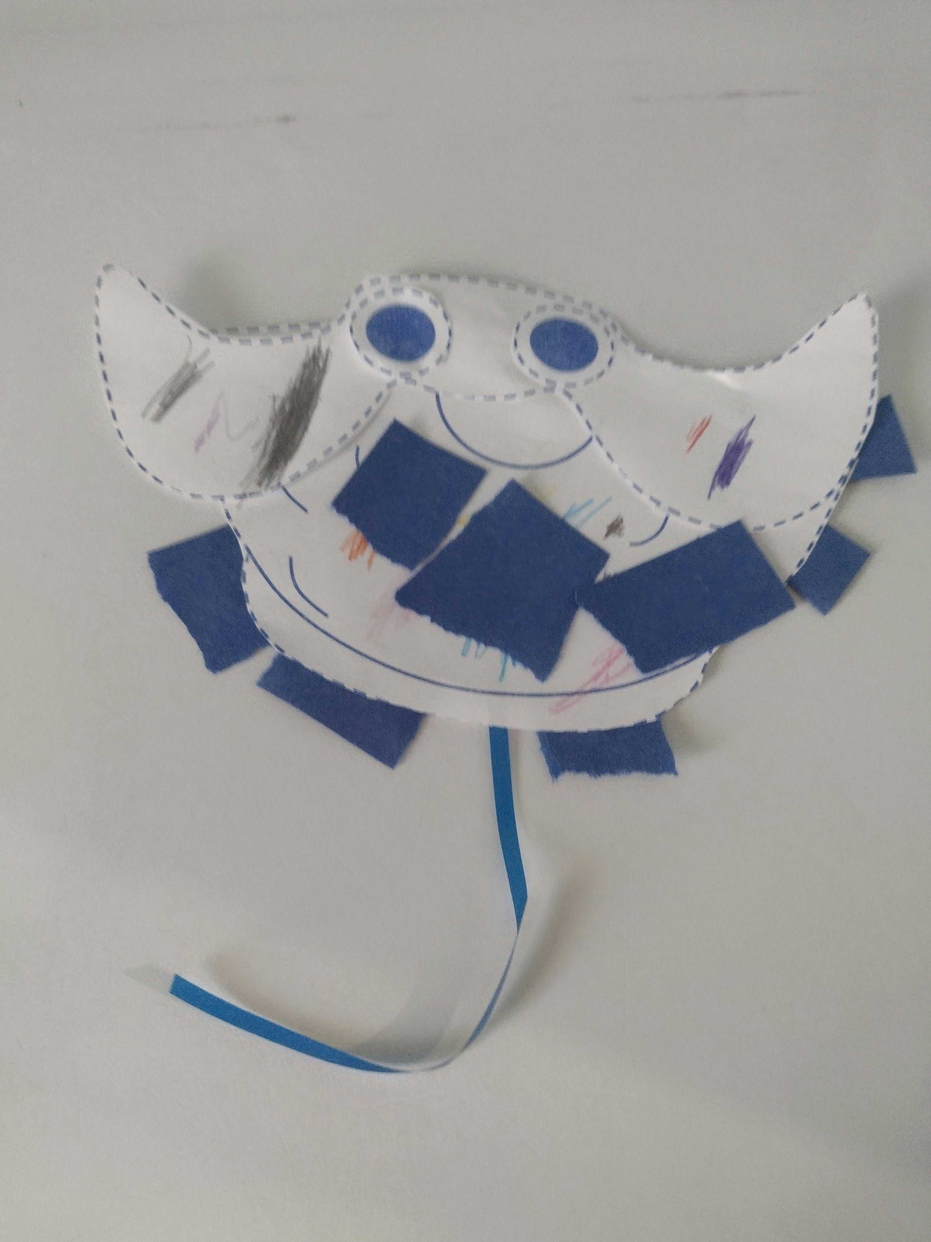 Paper plate craft of a manta ray with blue paper squares and ribbon