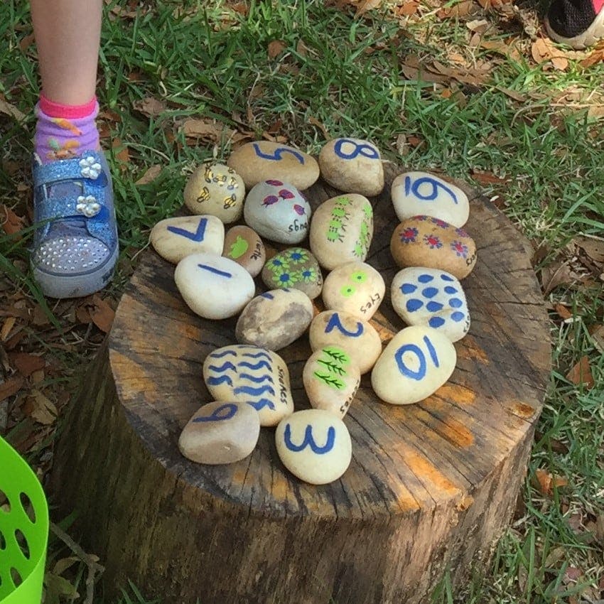 Child's foot next to painted rocks with numbers and patterns on a tree stump