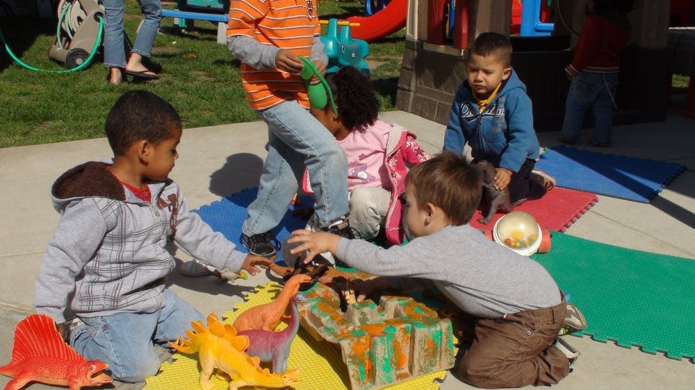 Children playing with toy dinosaurs on a mat outdoors