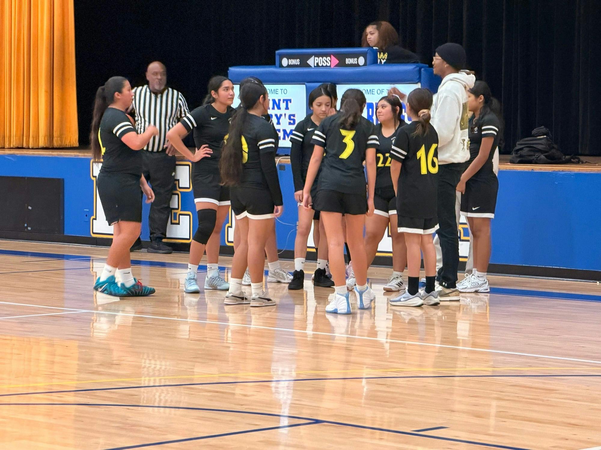 A group of people in black and yellow uniforms on a basketball court with a referee