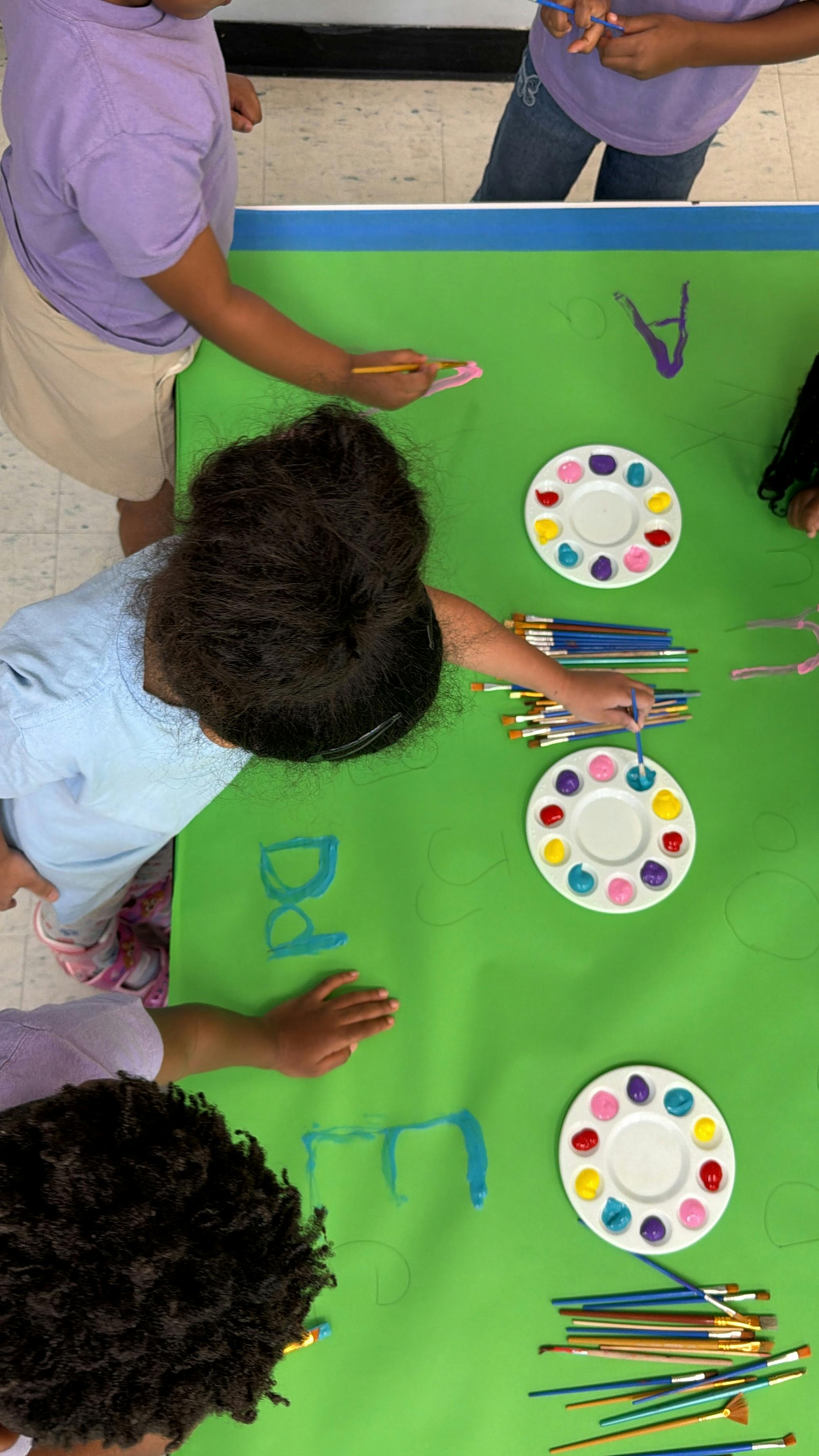 Children painting letters on a large green paper sheet