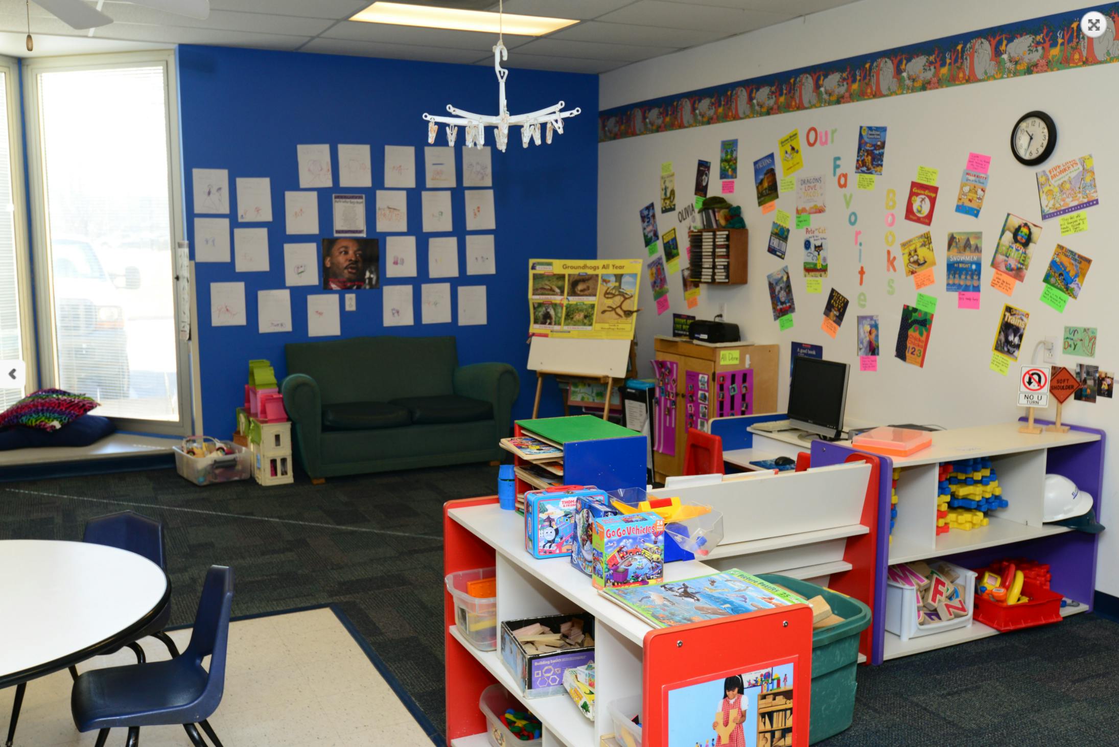 Classroom with blue and white walls, shelves with toys, and a small sofa