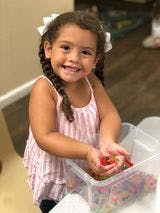 Child holding small objects over a clear bin