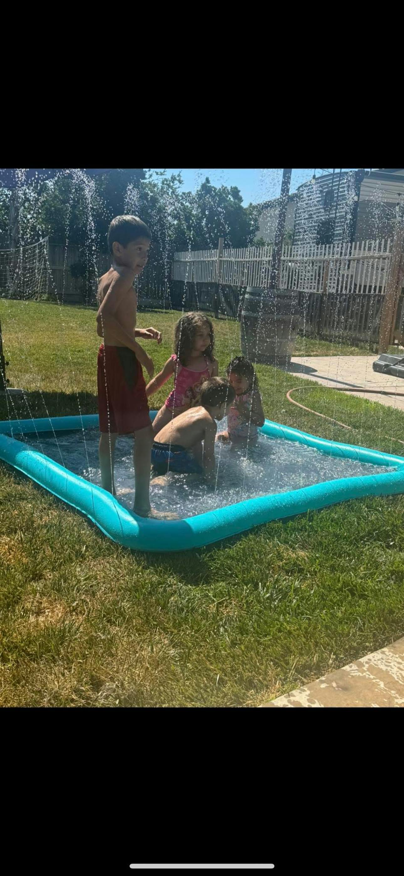 Children playing in a small inflatable pool with water spraying over them