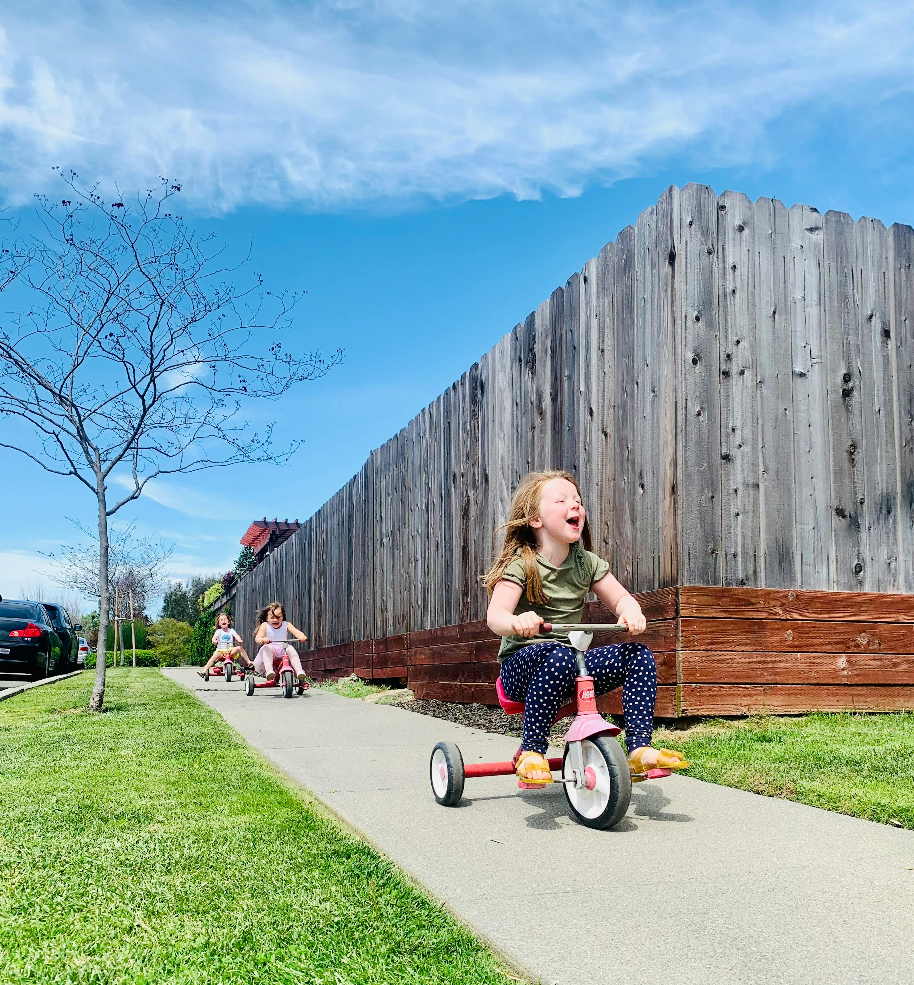 Child riding a tricycle on a sidewalk with other children in the background