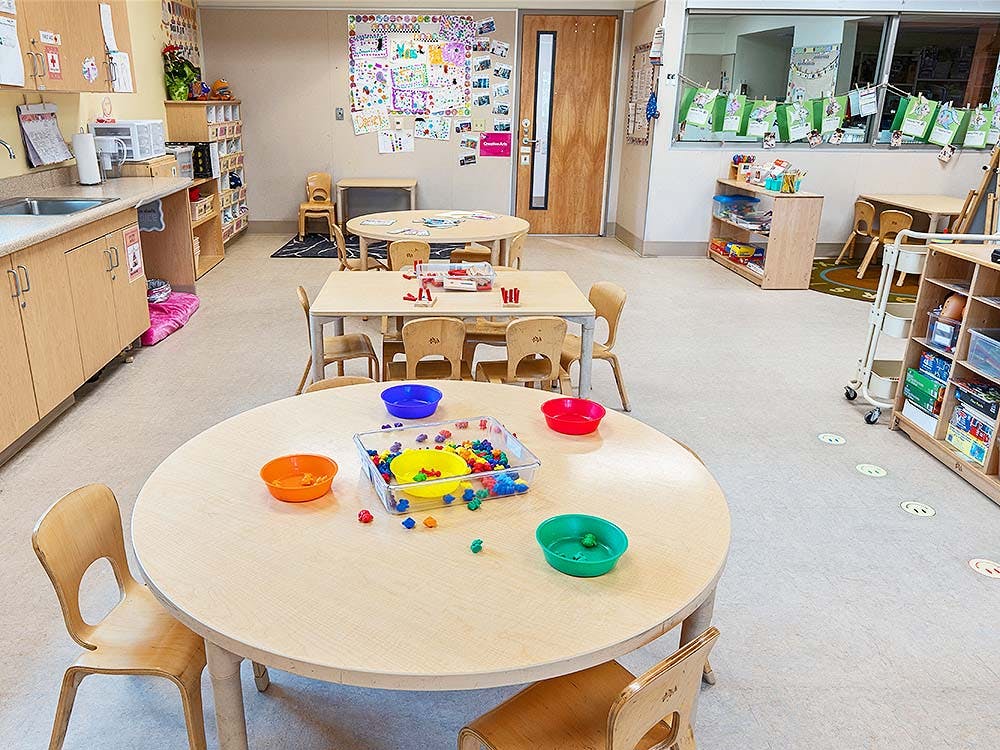 Classroom with small tables and chairs, sink, shelves, and artwork on walls