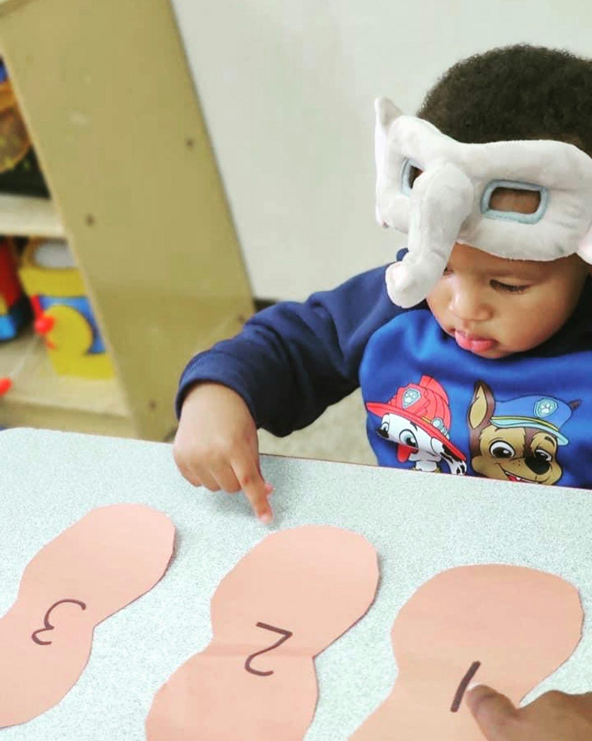 Child in elephant mask pointing at paper cutouts with numbers