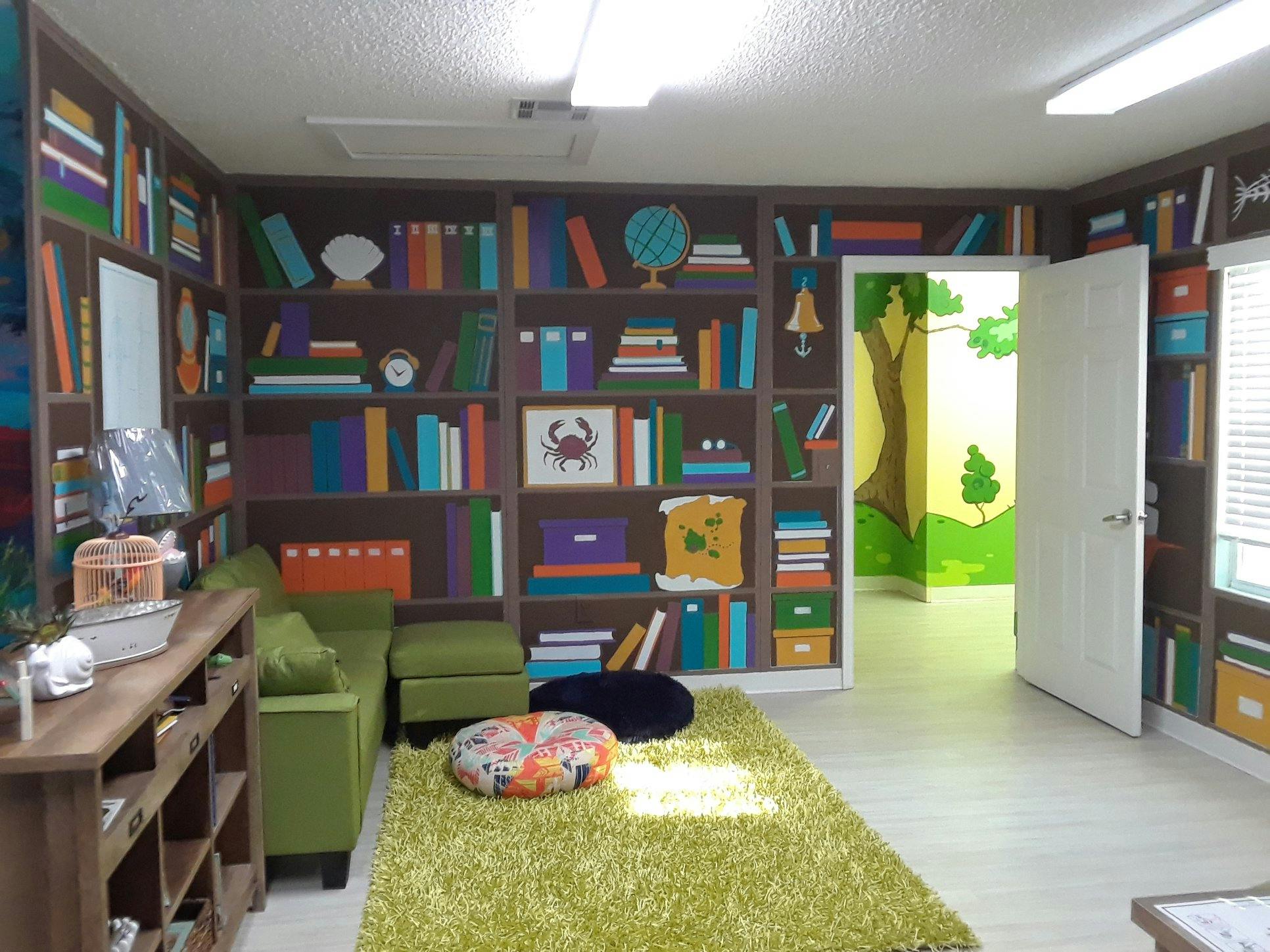 Room with bookshelf mural, green sofa, shag rug, and open door to nature mural