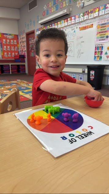 Child playing with a color wheel and small animal figures in a classroom