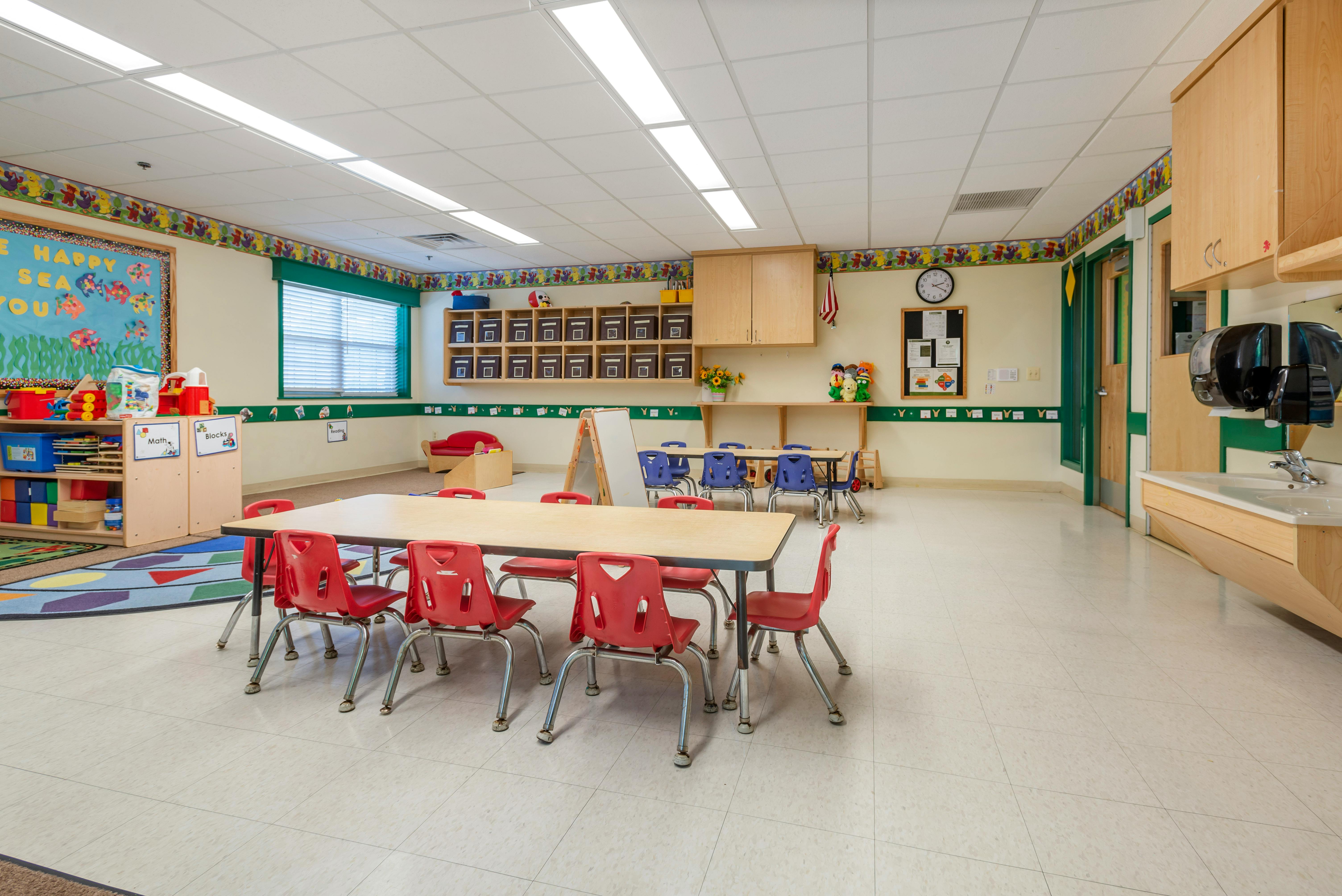 Empty classroom with tables and chairs, learning materials, and a sink