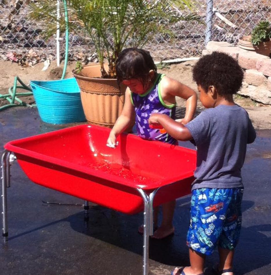 Two children playing with water in a red bin