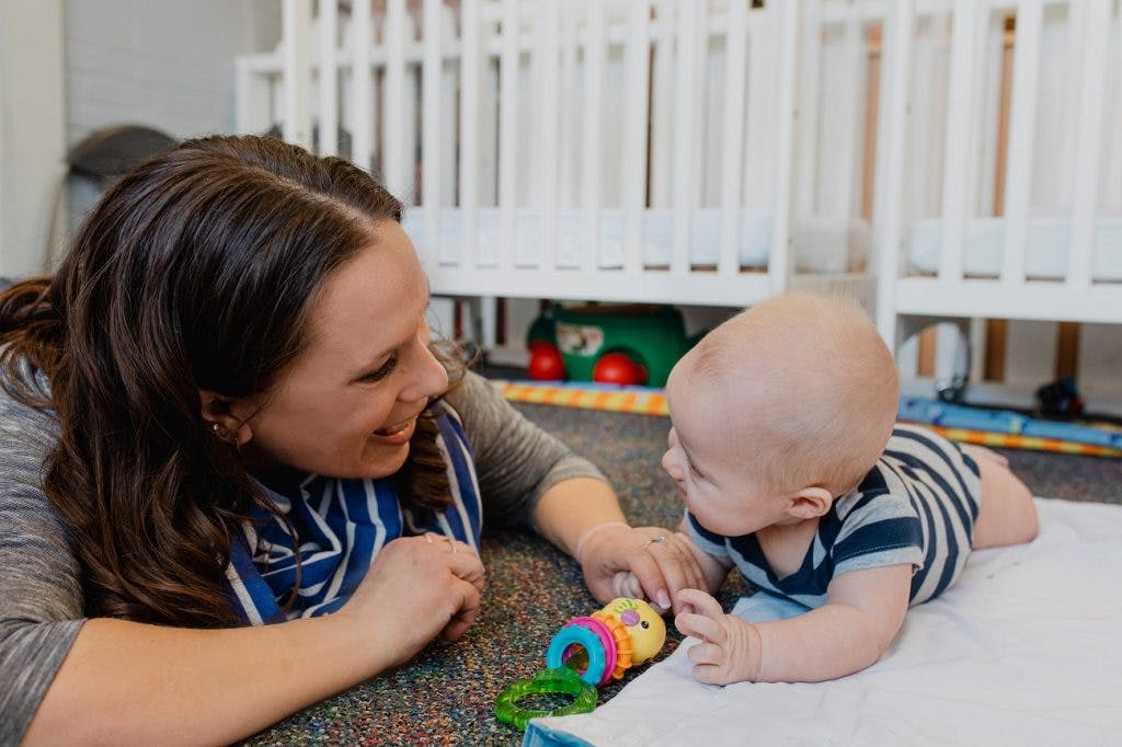 Person lying on floor interacting with a baby playing with a toy