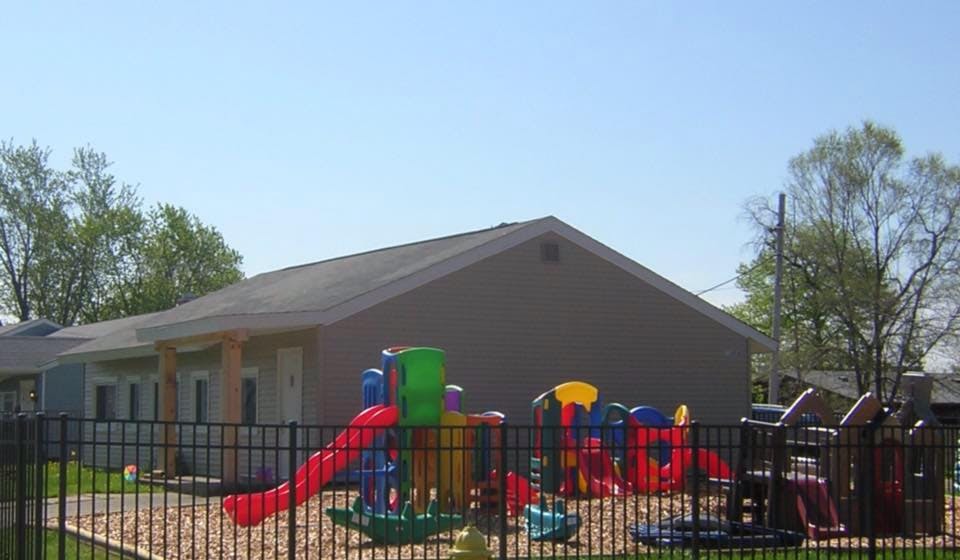 Playground with colorful equipment behind a fence, next to a building