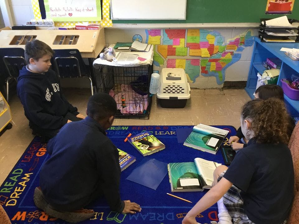 Three children sitting on a blue rug with books in a classroom