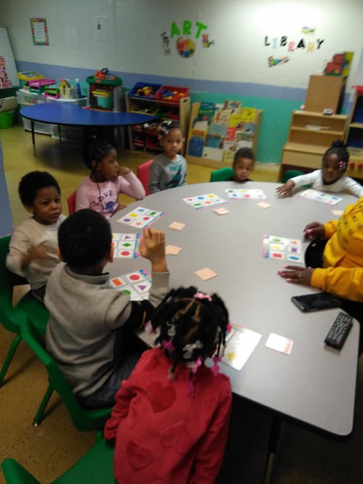 Children and an adult sitting around a table with cards in a classroom