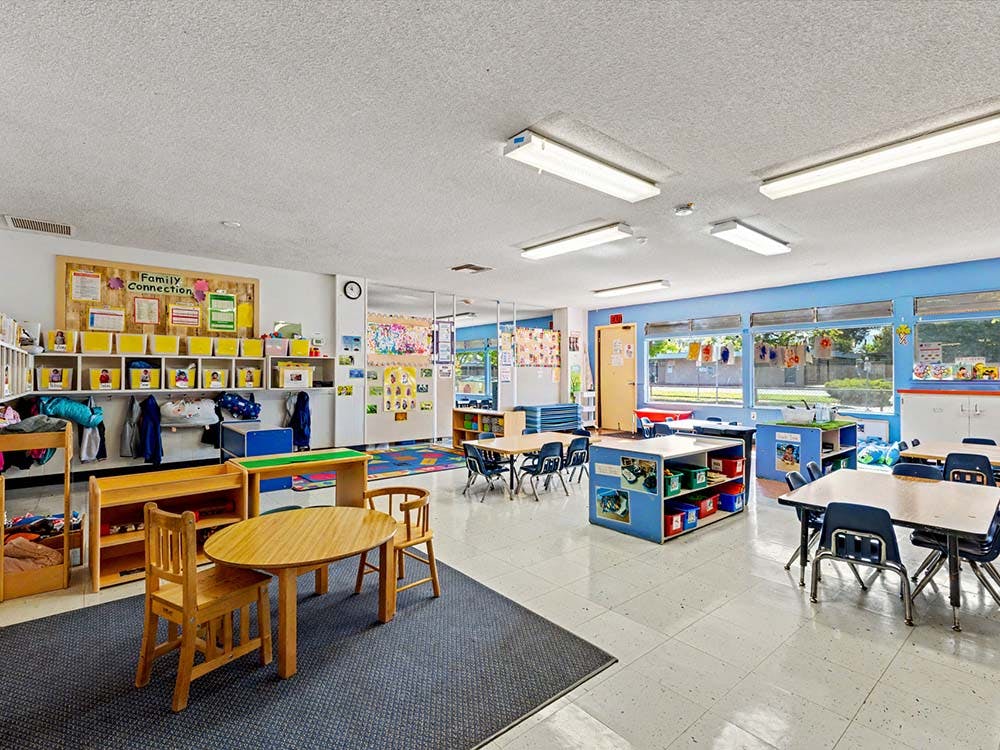 Empty classroom with small tables and chairs, shelves, and large windows