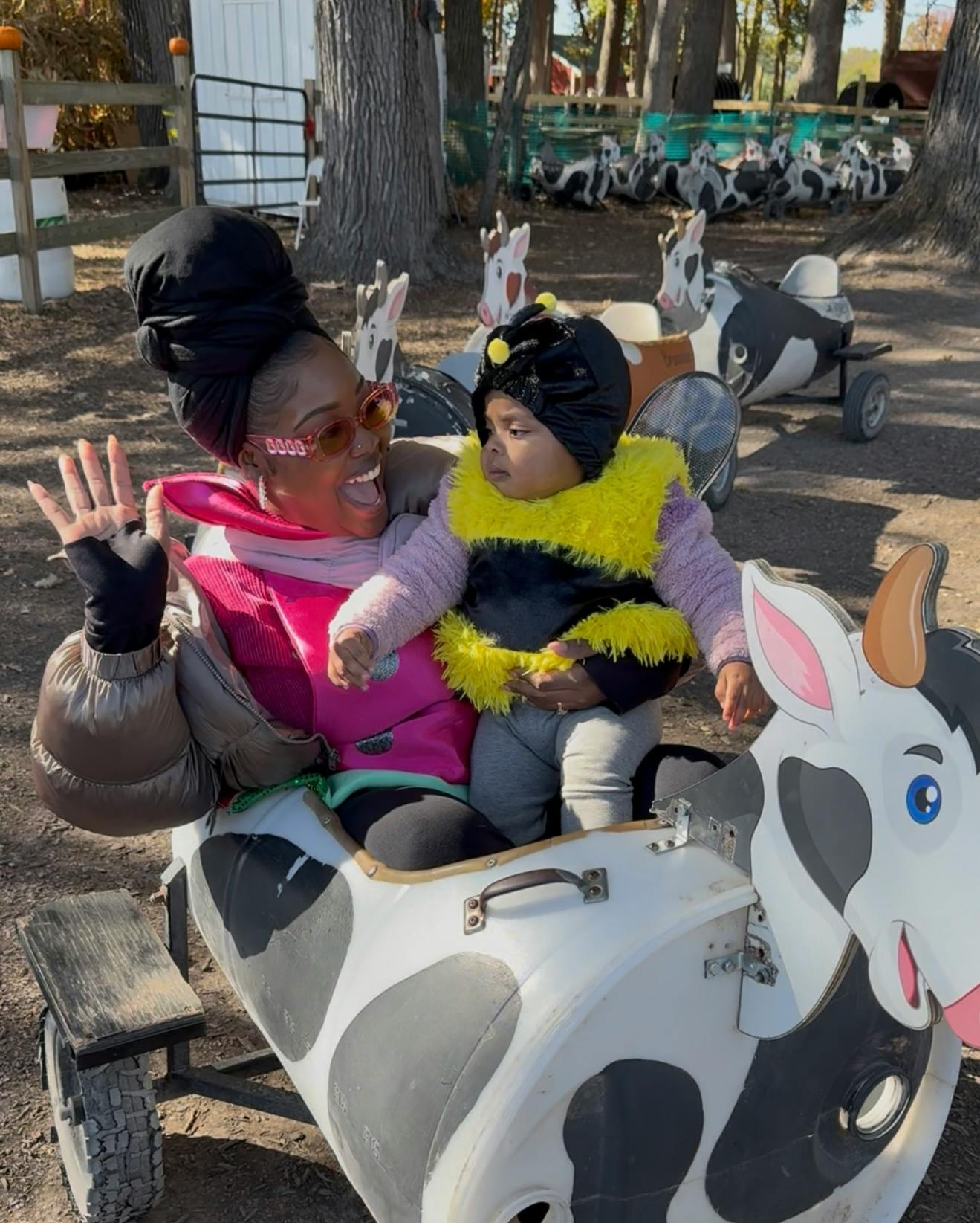 Person holding a child in a bee costume in a cow-shaped cart