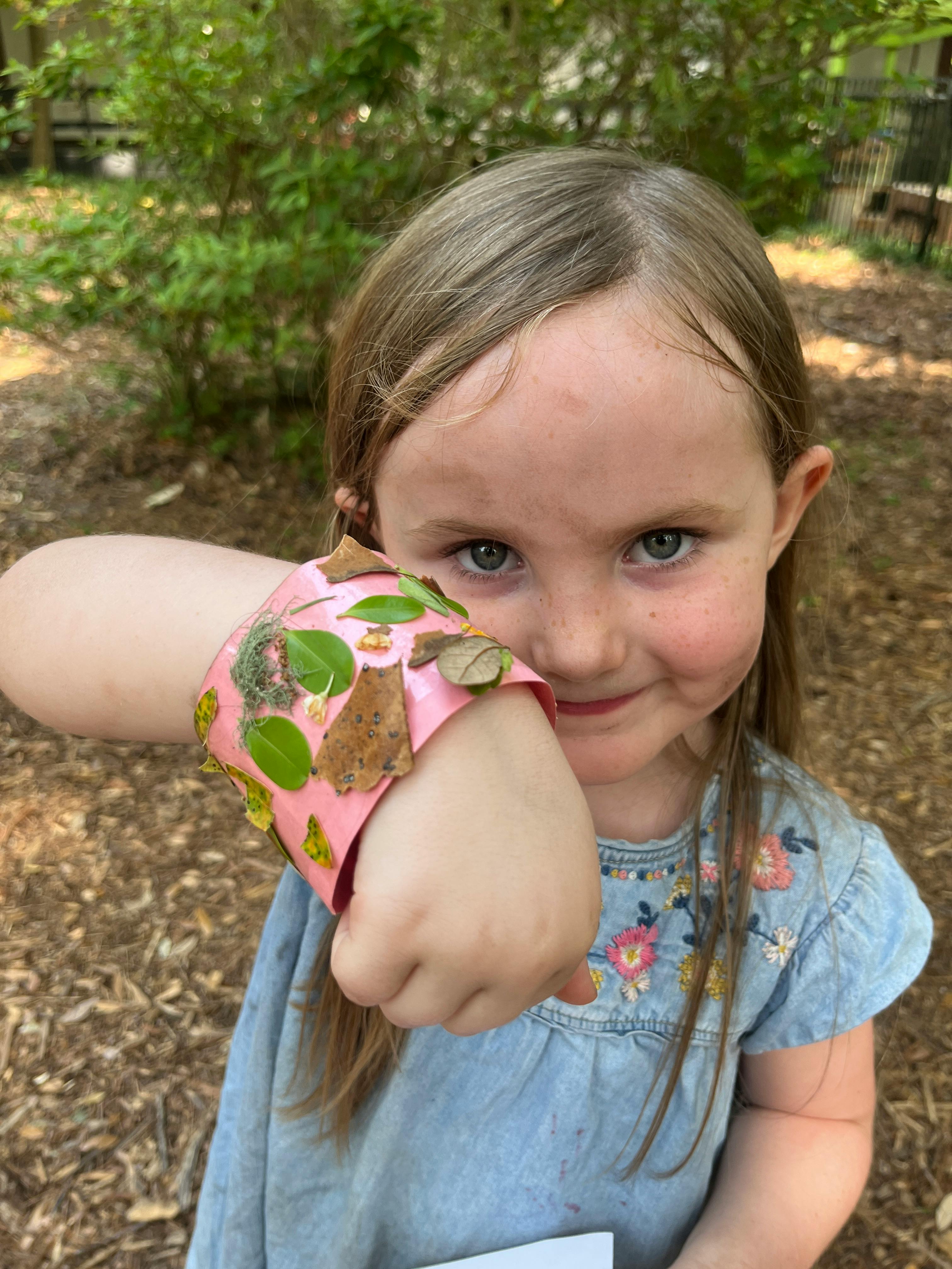Child with a pink bracelet decorated with leaves and bark