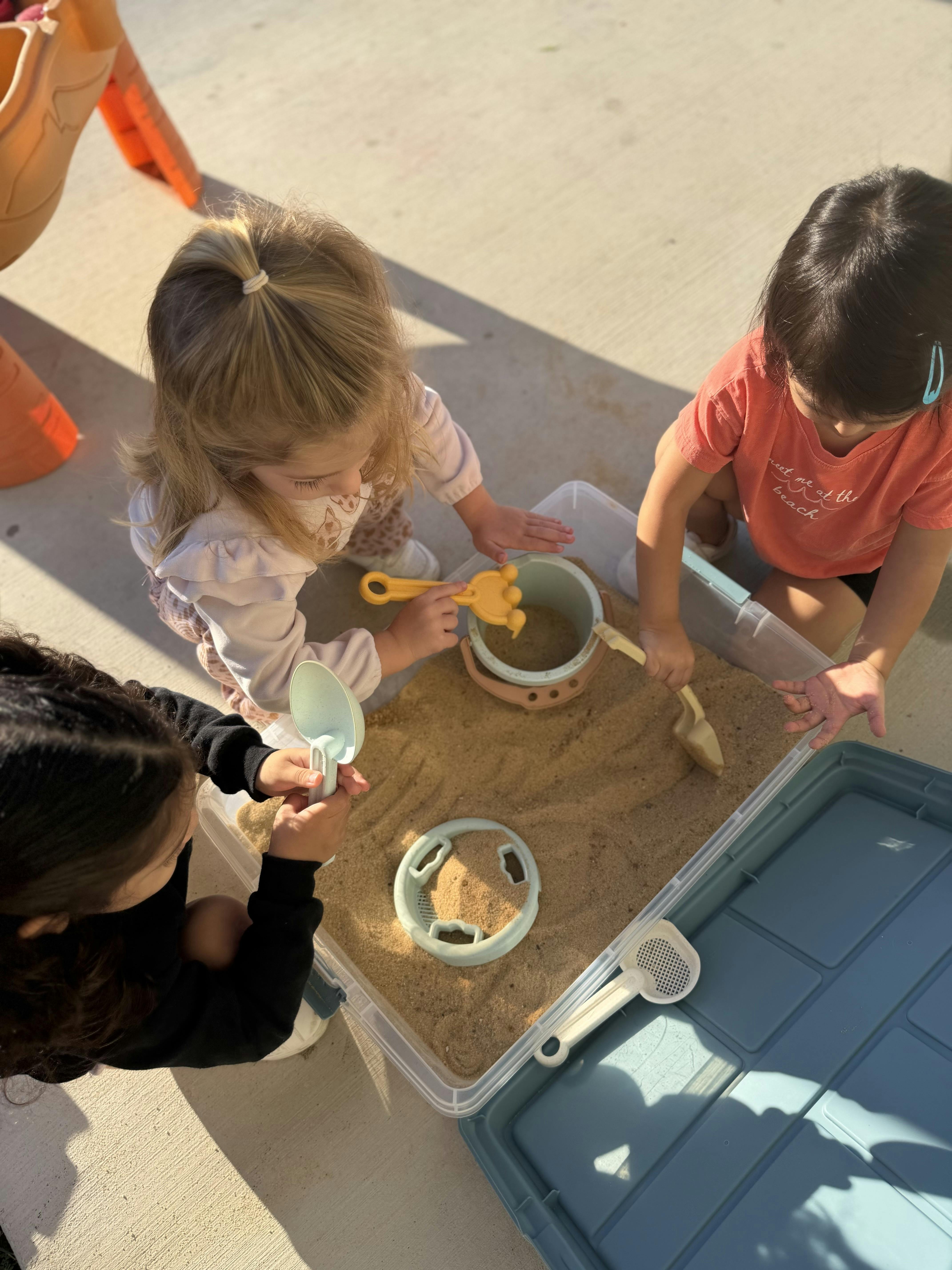 Three children playing with sand and toys in a sand table