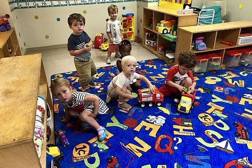 Children playing with toys on an alphabet rug in a classroom
