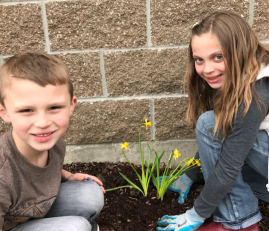 Two children planting flowers in a garden