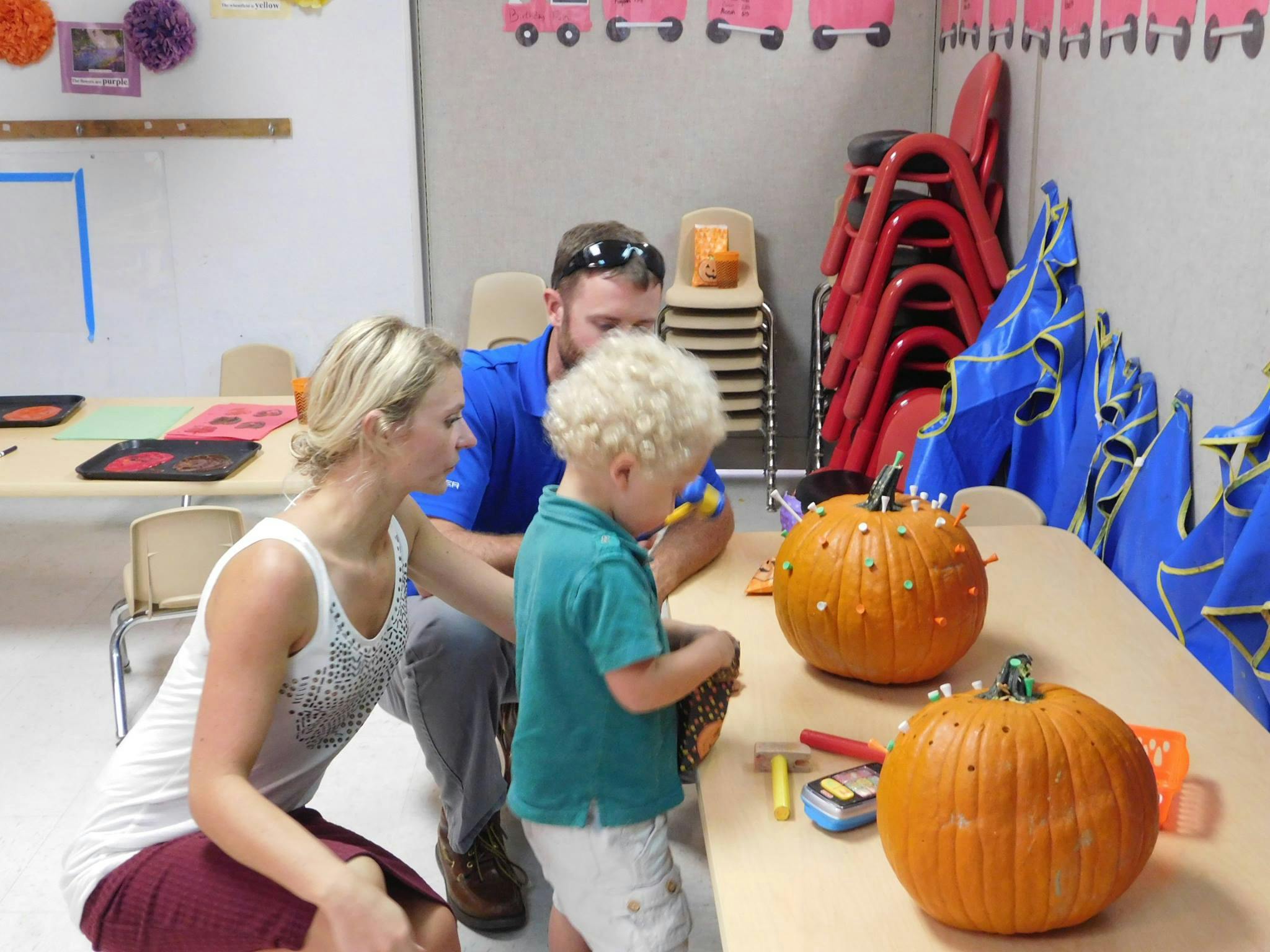 Two adults and a child decorating pumpkins at a table