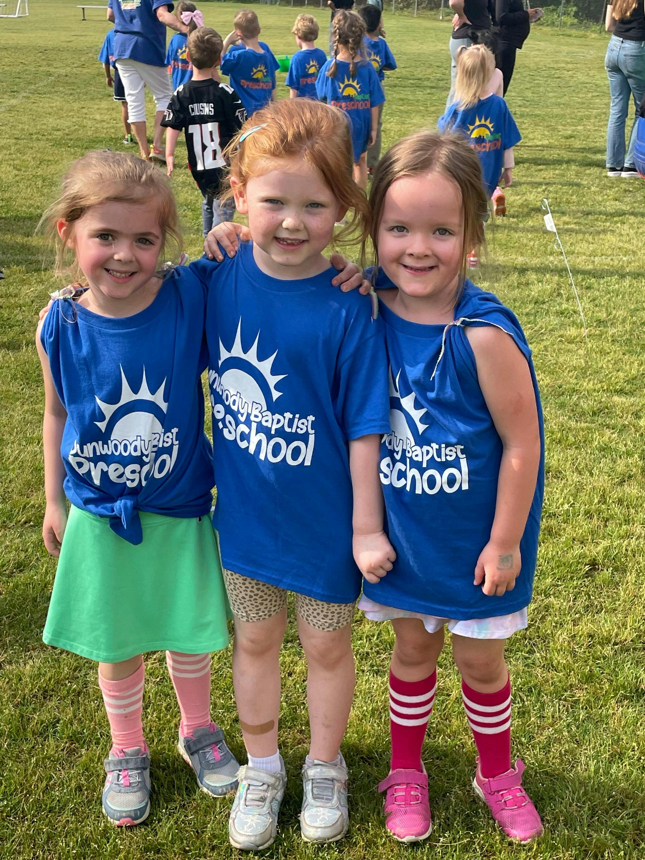 Three children in matching blue shirts standing on a grassy field