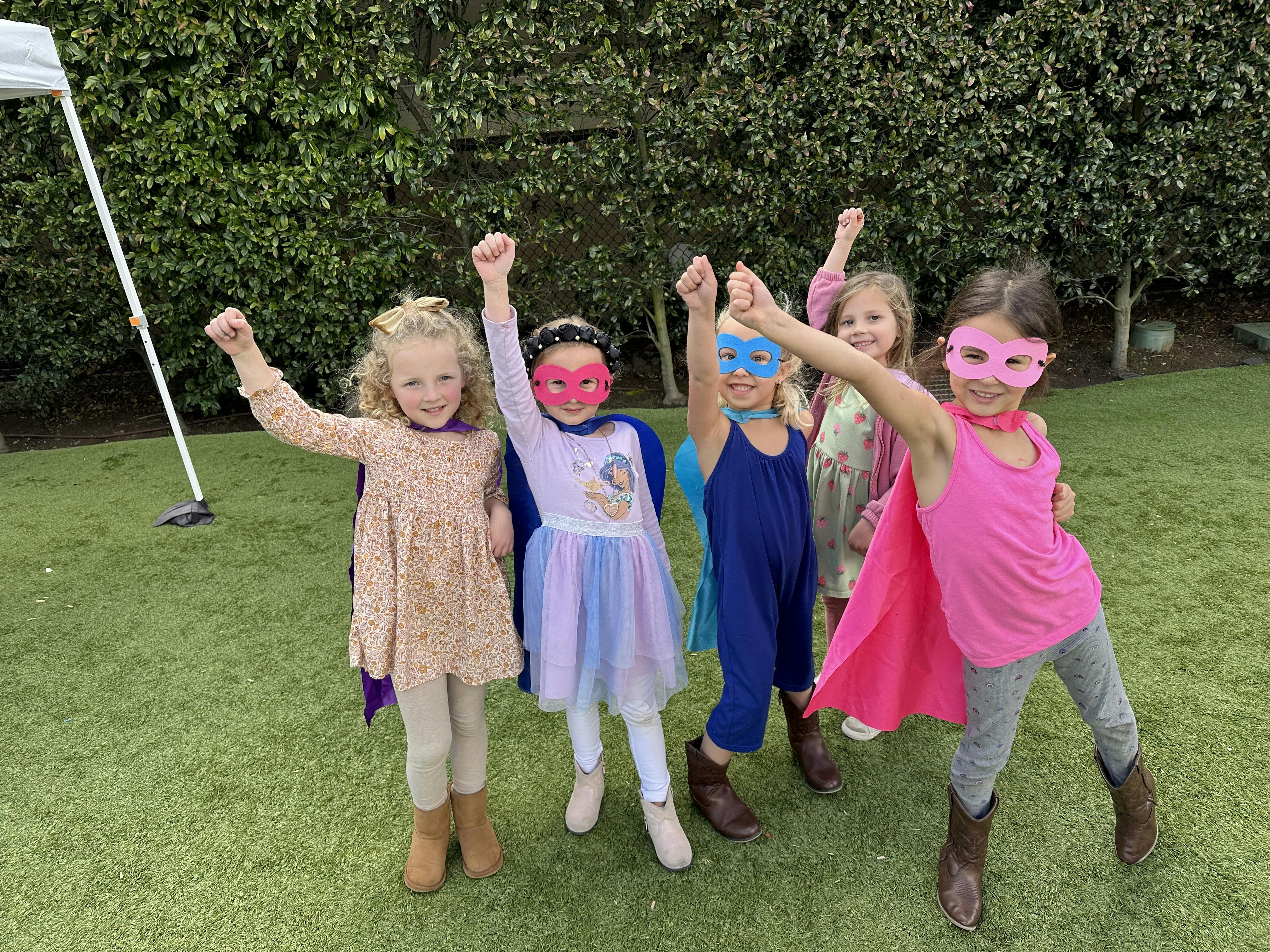 Group of children wearing superhero masks and capes raising their fists