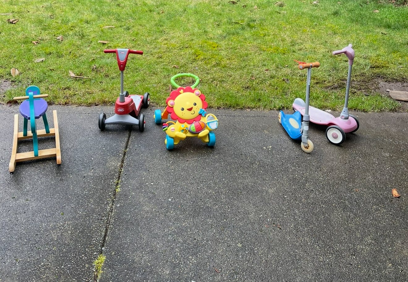 Children's toys including a wooden rocking horse, a lion-themed walker, and scooters