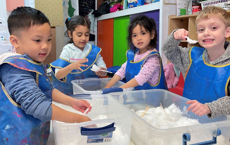 Four children in smocks playing with white sensory materials in clear bins