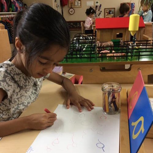 Child drawing on paper at a table in a classroom