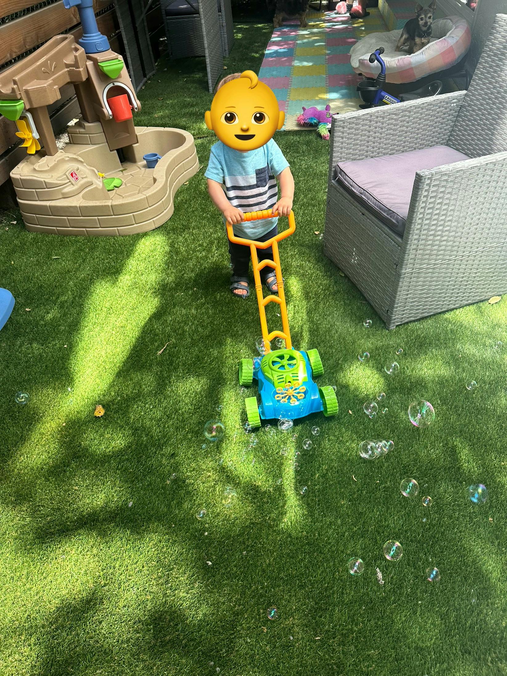Child pushing a toy bubble mower on green artificial grass