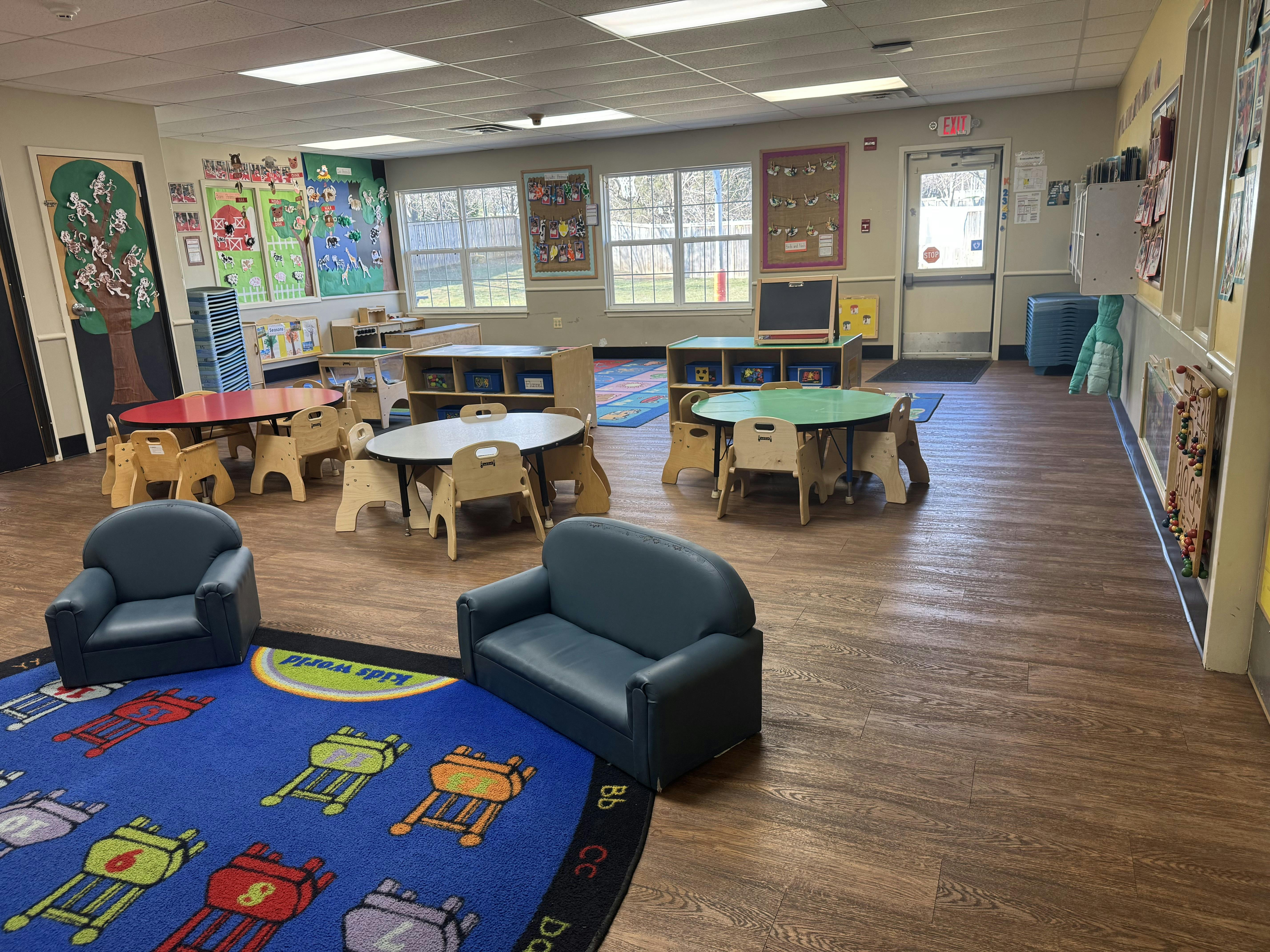 Classroom with several small tables and chairs, a blue rug, and wall decorations