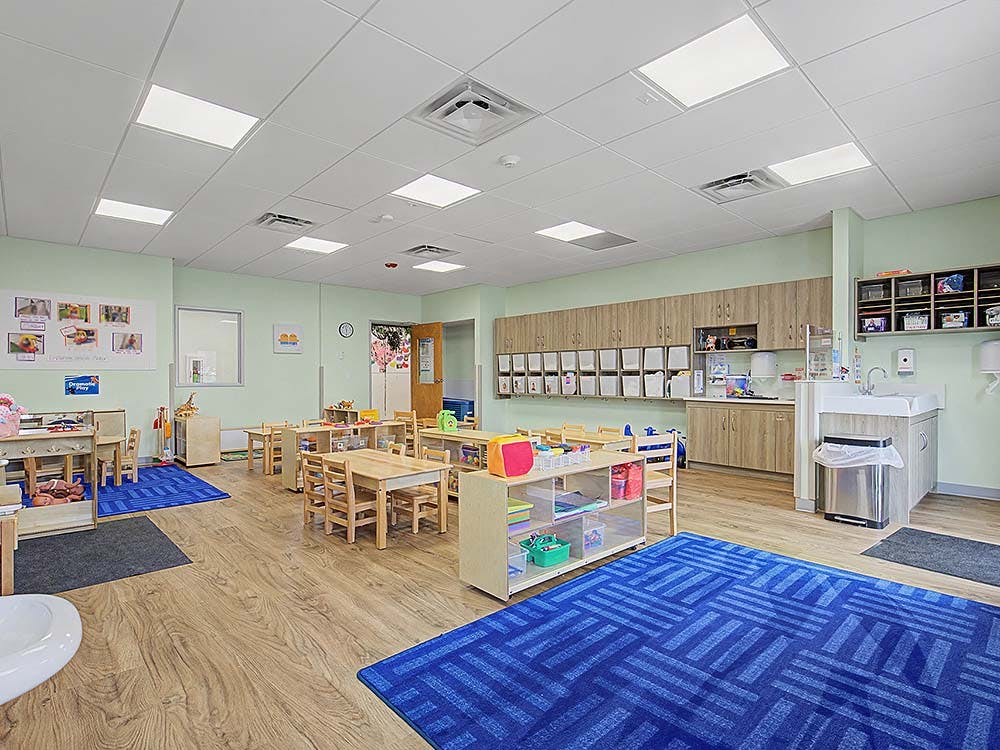 Empty classroom with small wooden tables and chairs, and blue rugs