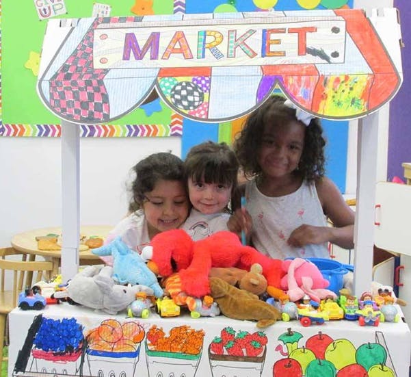 Three children behind a play market stand with stuffed animals