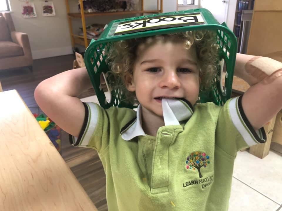 Child with a green basket on their head and a spoon in their mouth