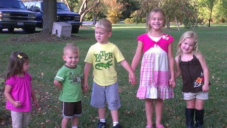 Five children standing on grass, two holding hands