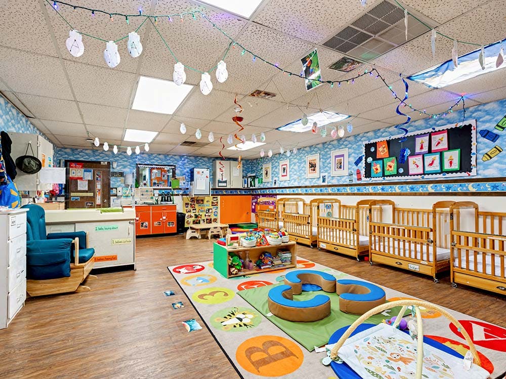 Baby room with multiple wooden cribs, a rocking chair, and play mats