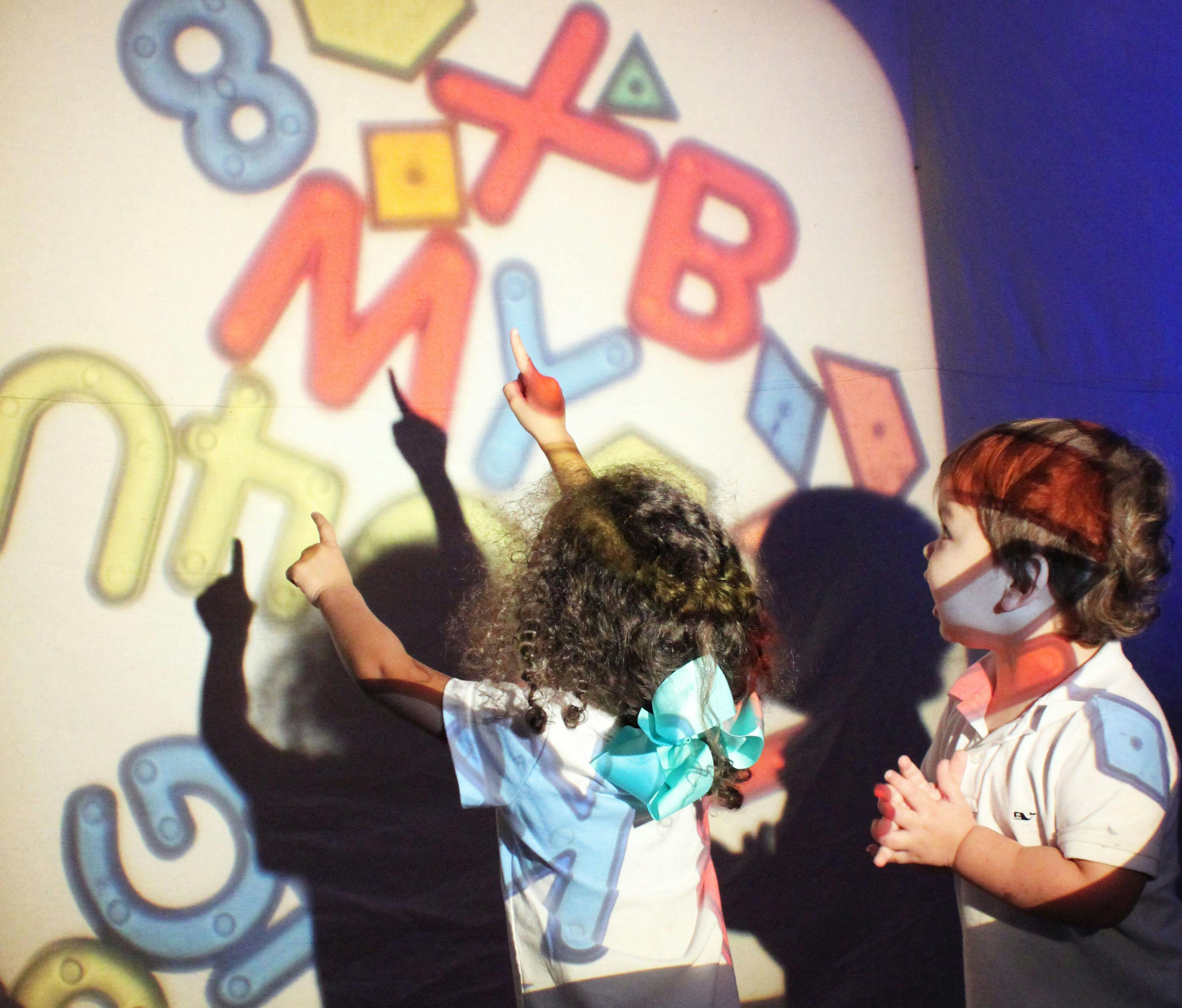 Two children pointing at projected letters and numbers