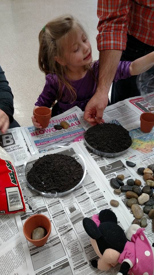 Child and person planting in small pots with soil and rocks
