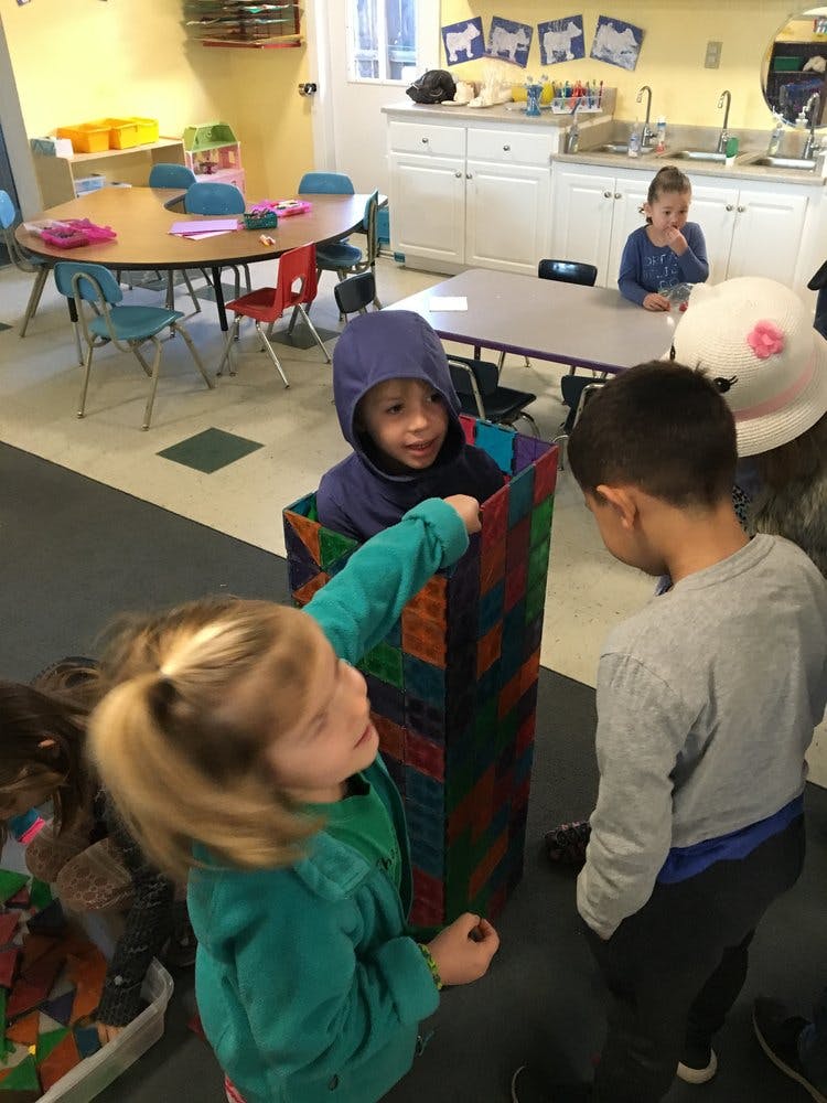Child in a colorful box interacting with another child in a classroom