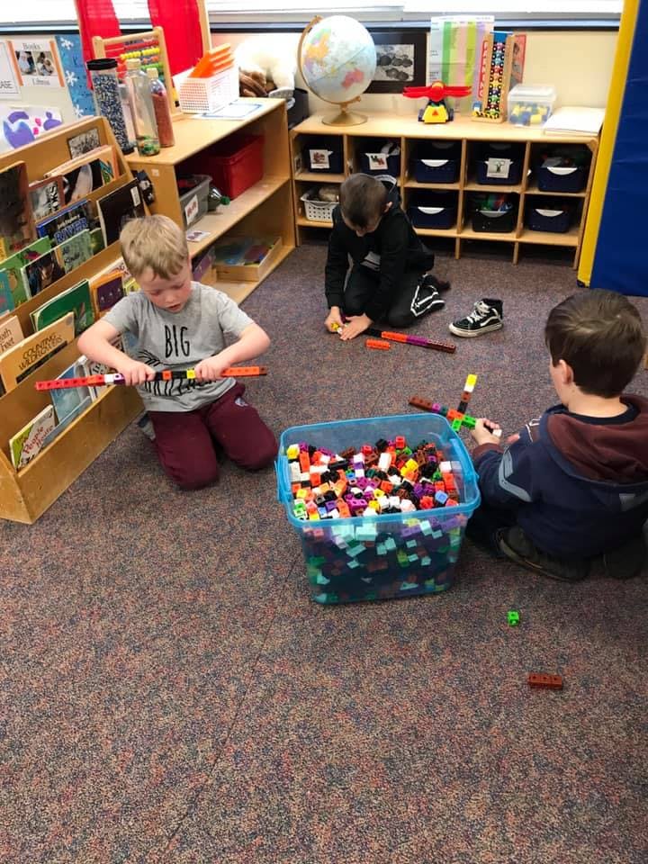 Three children playing with colorful building blocks in a classroom