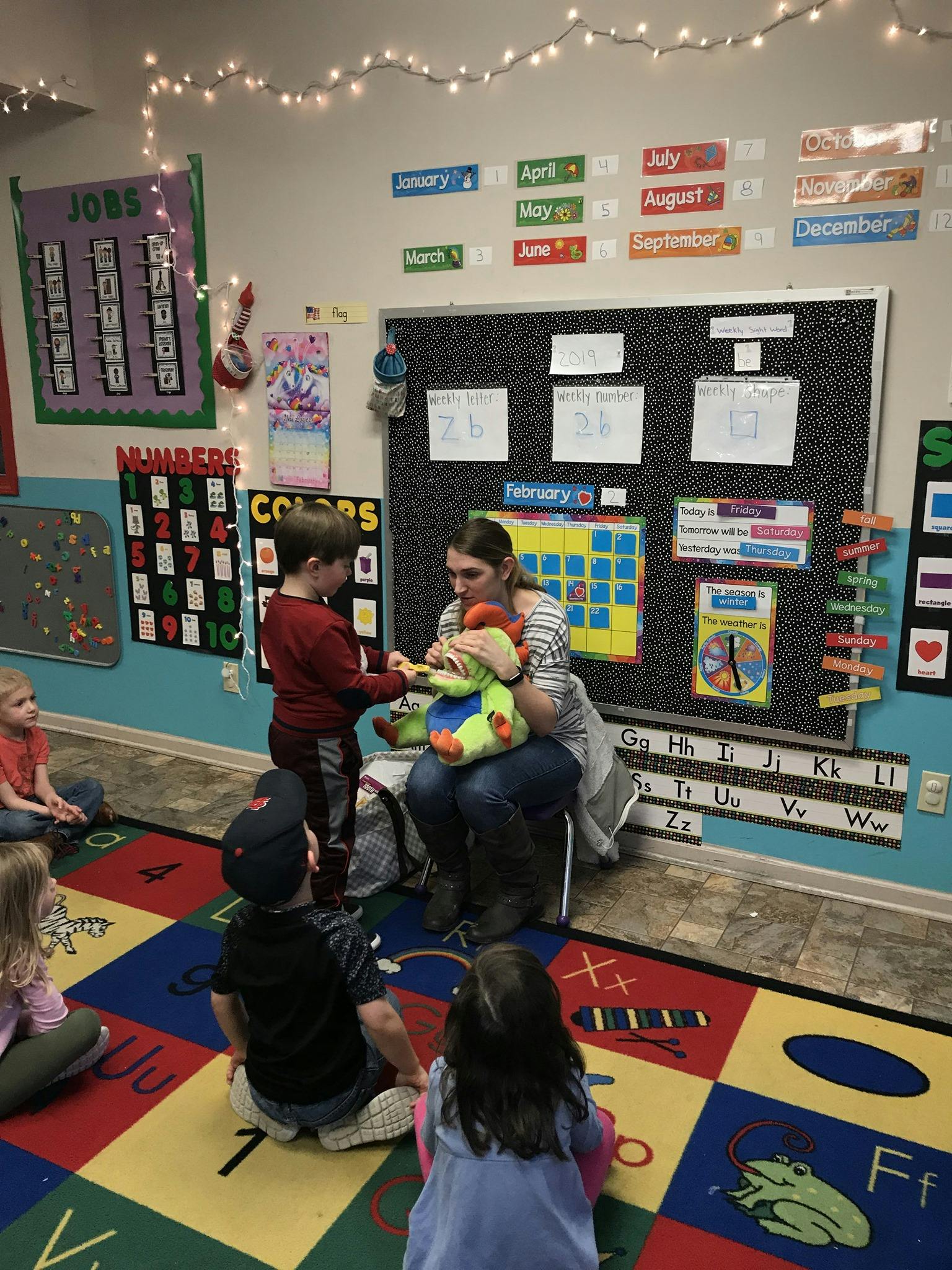 Adult and children interacting with a stuffed animal in a classroom