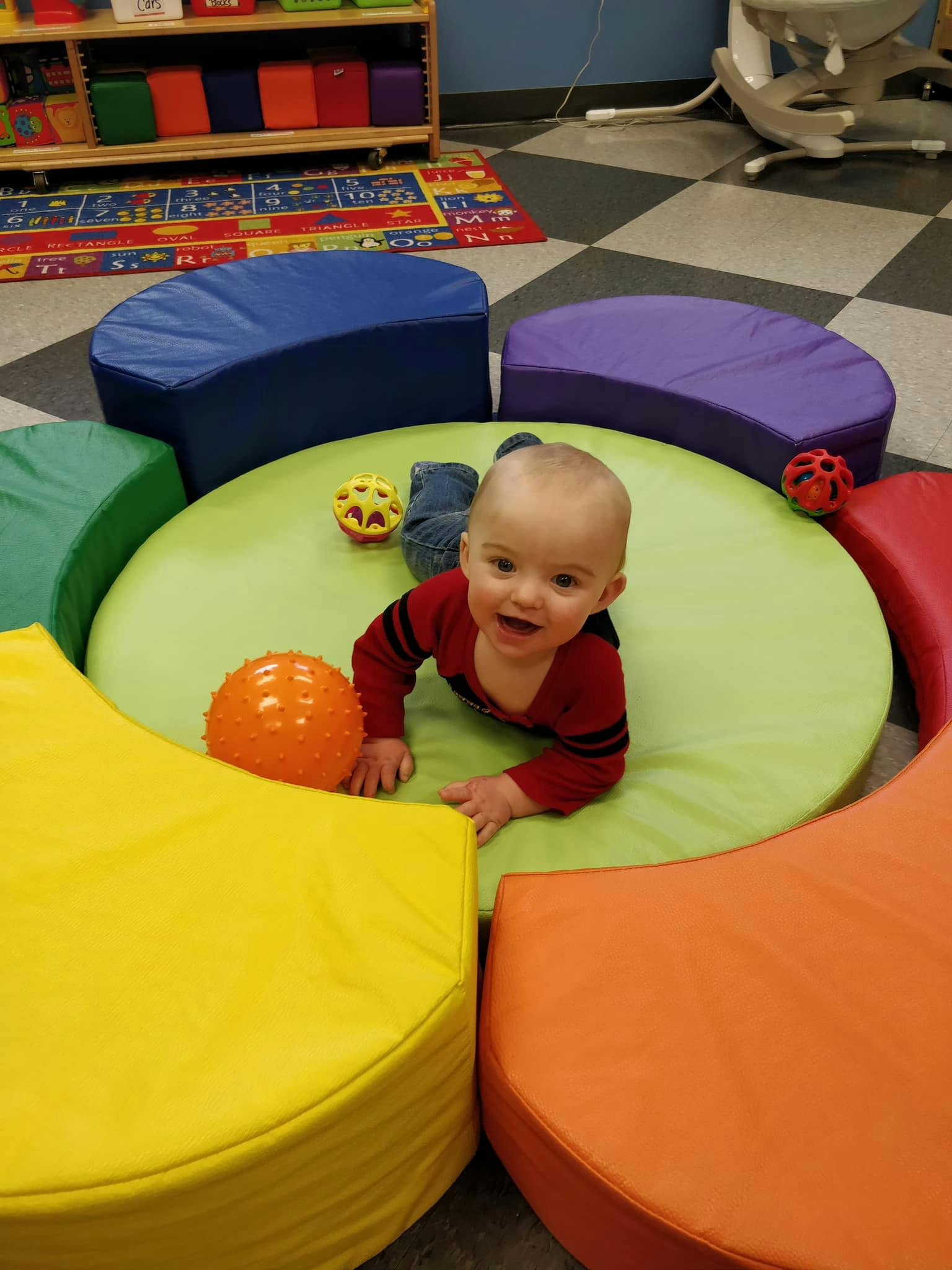 Child on a green mat surrounded by colorful soft seating