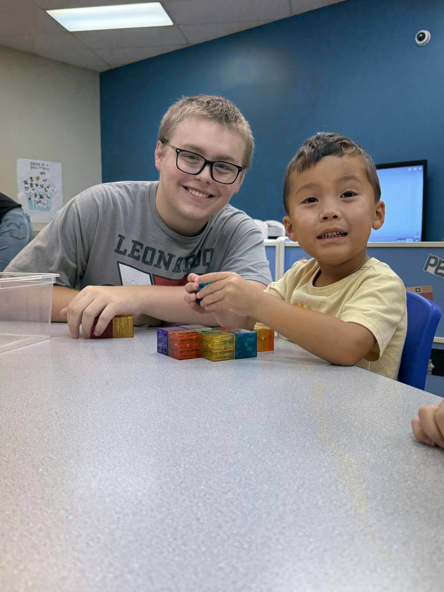 A teen and a child playing with magnetic blocks at a table