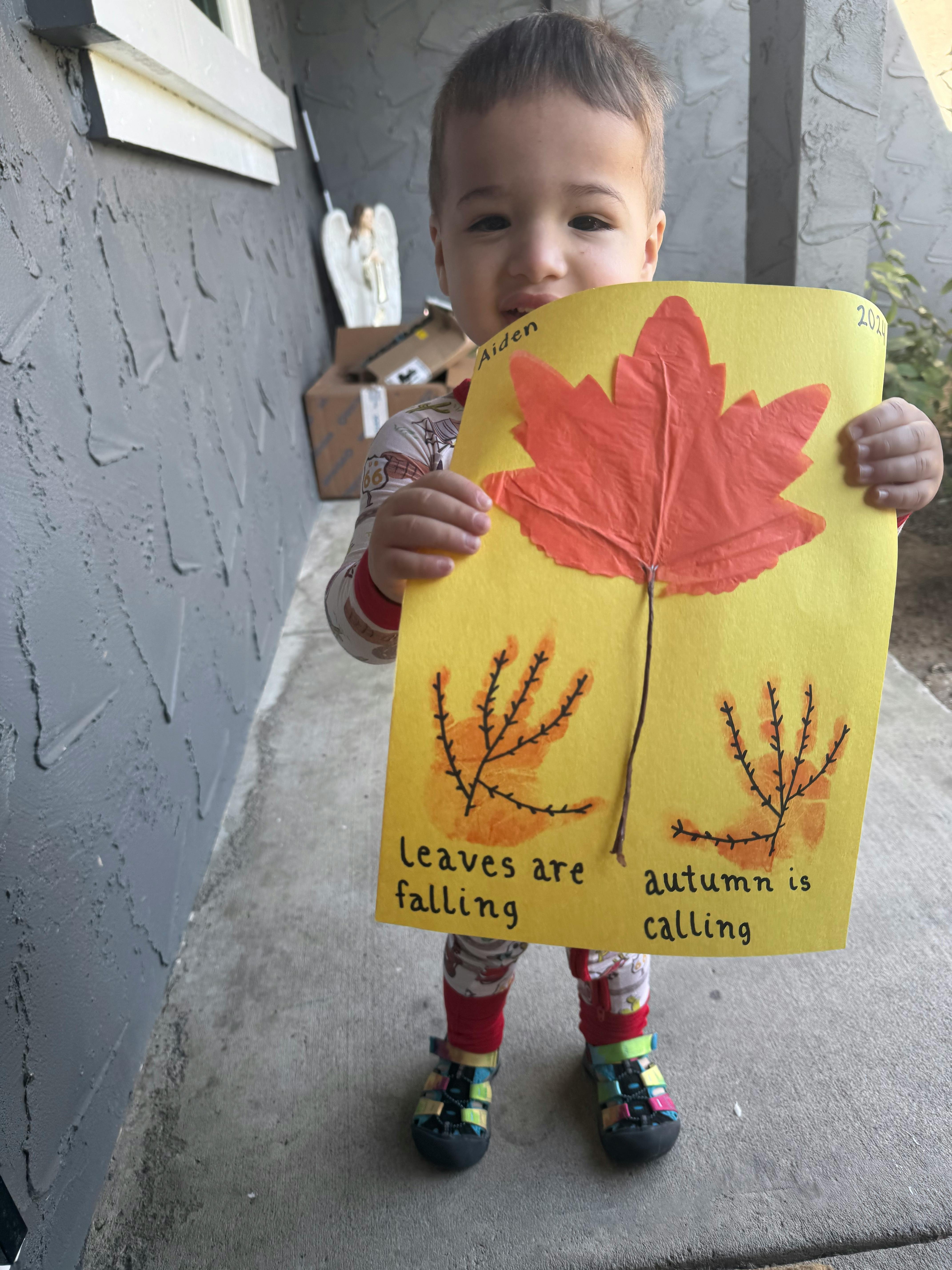 Child holding up a yellow paper with a red leaf and text about autumn