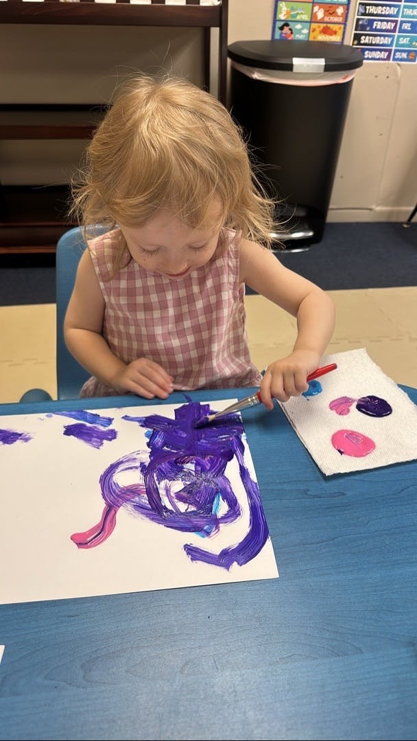 Child painting on paper with purple and pink paint