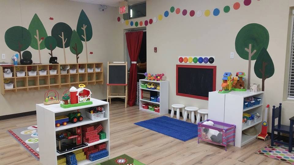 Classroom with shelves of toys, a chalkboard, and tree decals on the wall
