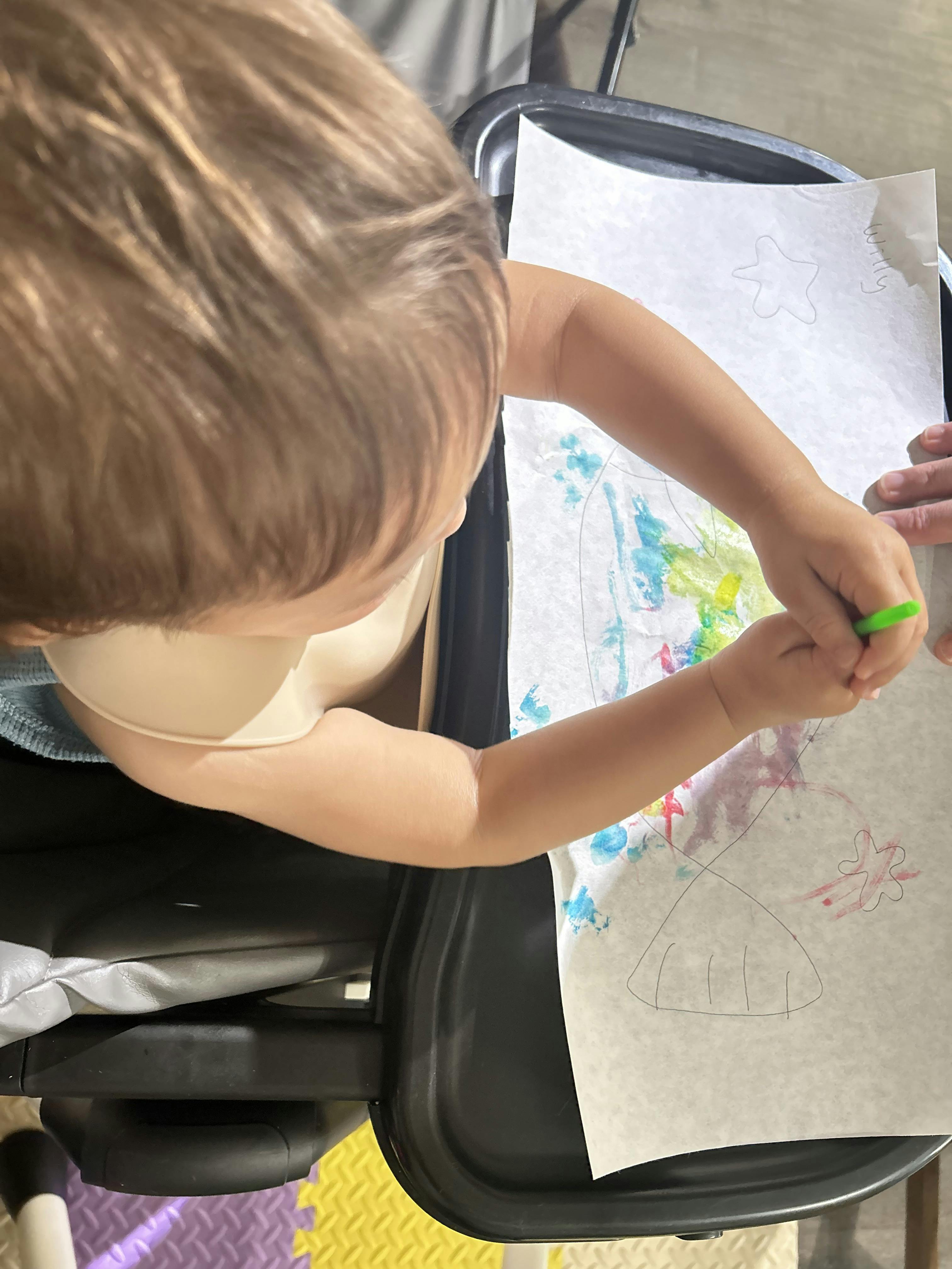 Child drawing with crayons on paper on a high chair tray