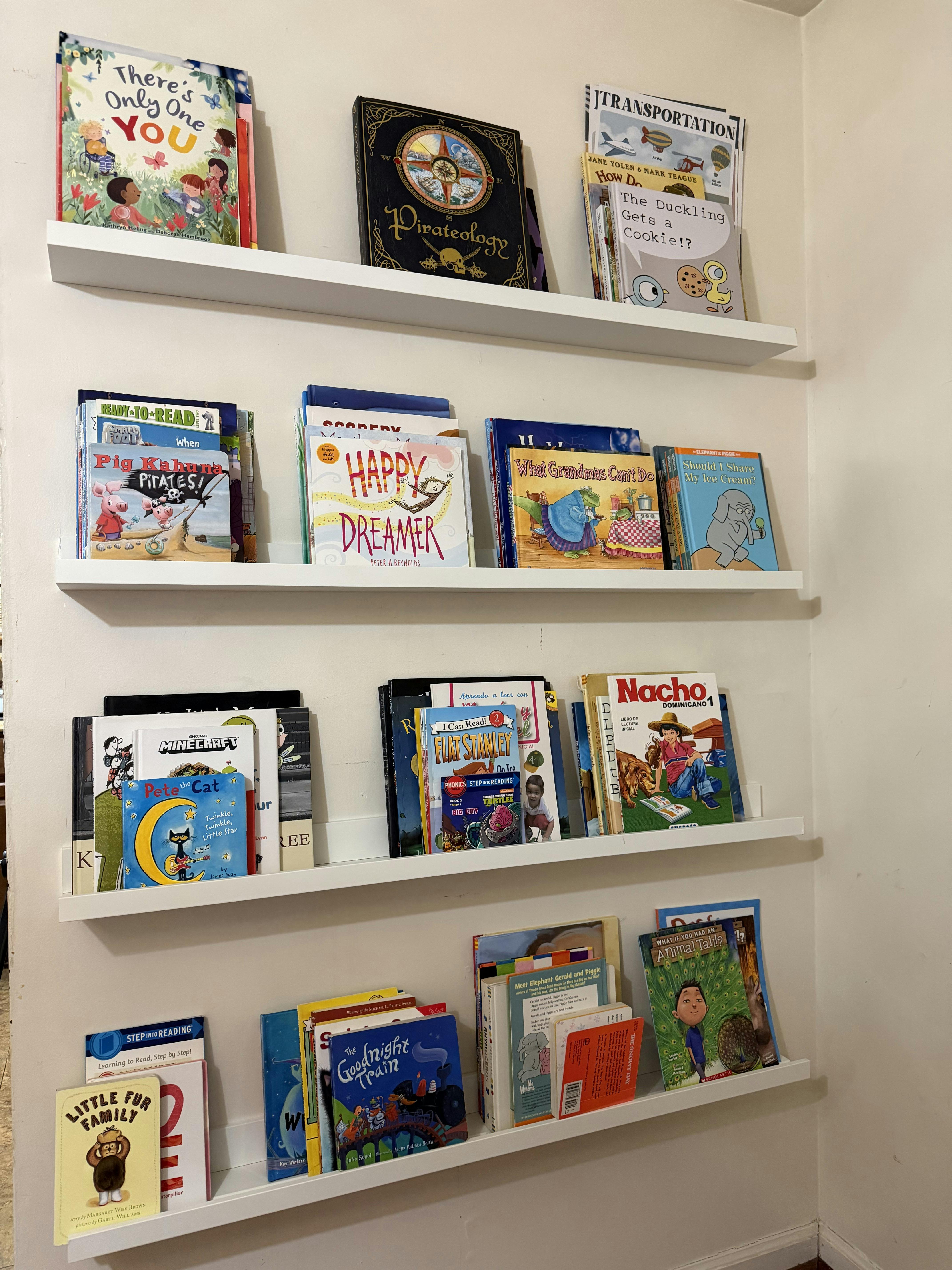 Four white wall shelves displaying a collection of children's books